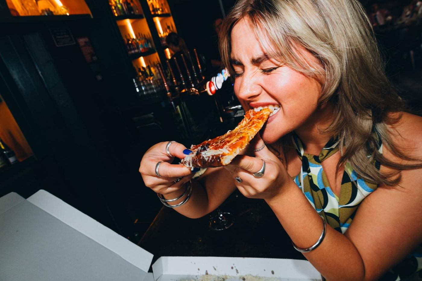 Someone taking a big bite of a slice at the bar