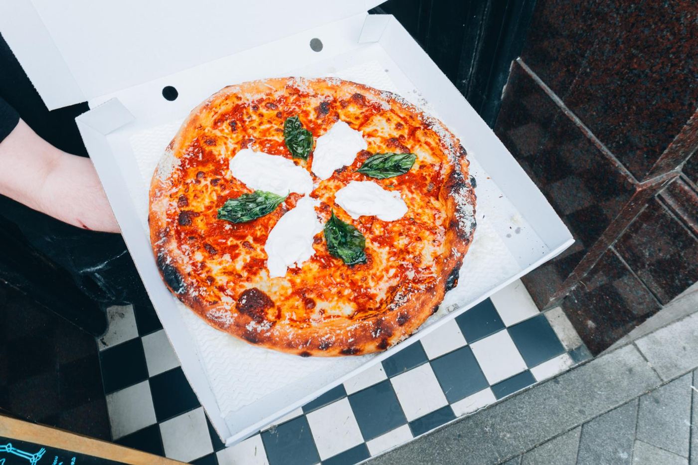A pizza in a white box held over a tiled doorstep