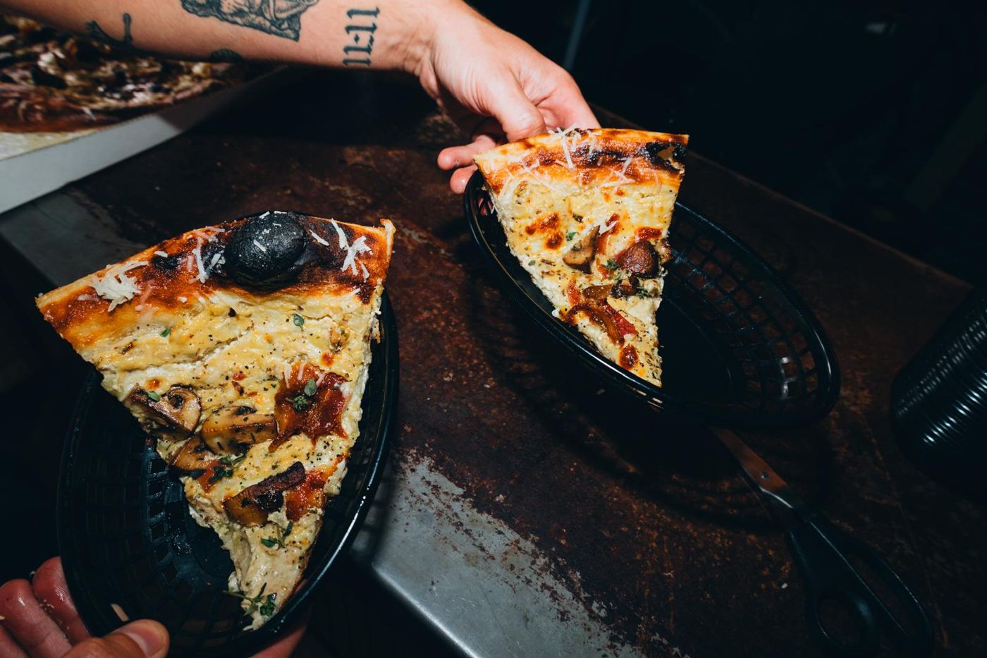 Two white pizza slices with mushrooms in black baskets